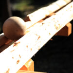 Eine Holzkugel wird auf zwei rauen, unbearbeiteten Holzbrettern im Freien in hellem Sonnenlicht platziert.