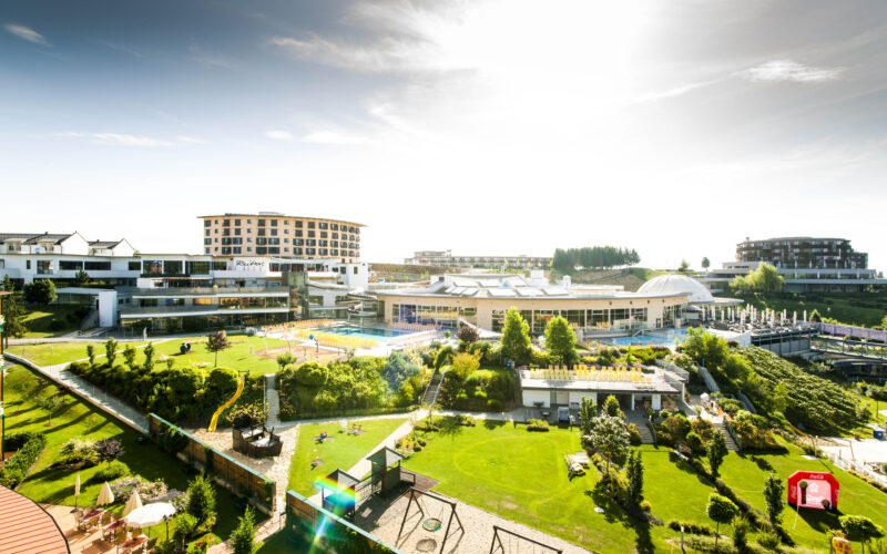 Ein großer Ferienkomplex mit mehreren Gebäuden, Außenpools, Gärten, Rasenflächen und Erholungsgebieten unter einem hellen, sonnigen Himmel.
