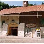 Ein rustikales Holzgebäude mit einem Uhrenturm mit der Aufschrift "Rappenlochmuseum Dornbirn" und einem Verkaufsautomaten in der Nähe des Eingangs.