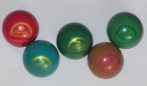 Fünf bunte Gummibälle mit goldenen Etiketten sind auf einer hellen Fläche angeordnet.