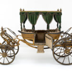 Elegante Vintage-Pferdekutsche mit grün drapiertem Vordach, getufteten Sitzen und detaillierten goldenen Akzenten, dargestellt vor einem schlichten weißen Hintergrund.