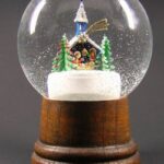 Eine Schneekugel mit Holzsockel und einer Miniaturkirche, Bäumen und Figuren im Inneren, umgeben von Kunstschnee.