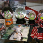 Ein Regal mit Schneekugeln, amerikanischen Flaggen, Figuren, Fotos und einer Schallplatte, die einen Mann in Reiterkleidung zeigt.