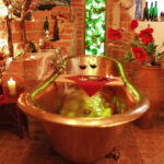 Eine mit Wasser gefüllte Kupferbadewanne, dekoriert mit Kerzen, roten Blumen, Weinflaschen und zwei Rotweingläsern auf einem Holztablett, in einem rustikalen Backsteinzimmer.