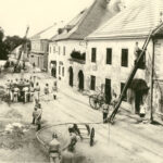 Feuerwehrleute in Uniform bekämpfen mit Leitern und Schläuchen einen Brand in einer von Altbauten gesäumten Straße, während Schaulustige zusehen.