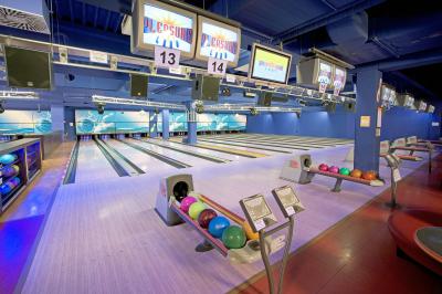 Eine hell erleuchtete Bowlingbahn mit mehreren Bahnen, bunten Bowlingkugeln auf Ständern und über jeder Bahn hängenden Bildschirmen für die Punktevergabe.