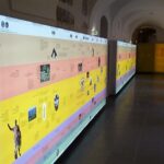 Eine lange, beleuchtete Zeitleiste mit Text und Bildern säumt die Wand eines Ganges in einem Museum oder Ausstellungsraum.