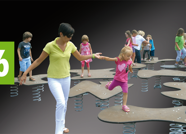 Ein Erwachsener hilft einem Kind, auf einer gefederten Spielplatzplattform das Gleichgewicht zu halten, während andere Kinder im Hintergrund spielen.