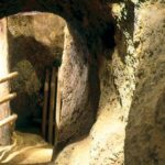 Ein schmaler, in den Fels gehauener Tunnel mit auf der linken Seite sichtbaren Holzgeländern, die mit künstlicher Beleuchtung beleuchtet werden.