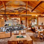 Ein gemütlicher Restaurantbereich mit Holzmöbeln, einem Buffet, dekorativen Deckengemälden und großen Fenstern, die natürliches Licht hereinlassen.