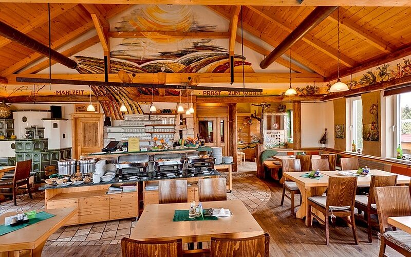 Ein gemütlicher Restaurantbereich mit Holzmöbeln, einem Buffet, dekorativen Deckengemälden und großen Fenstern, die natürliches Licht hereinlassen.