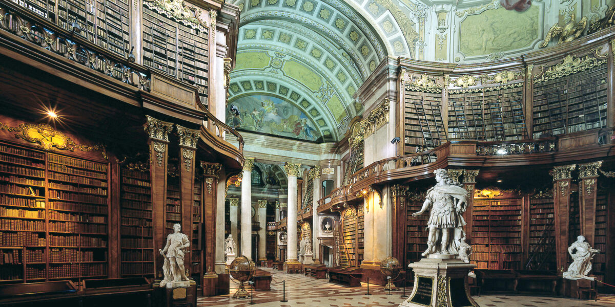Große, verzierte Bibliothek mit hohen, gewölbten Decken, detaillierten Fresken, hohen Bücherregalen, Marmorstatuen und einem gemusterten Fußboden.