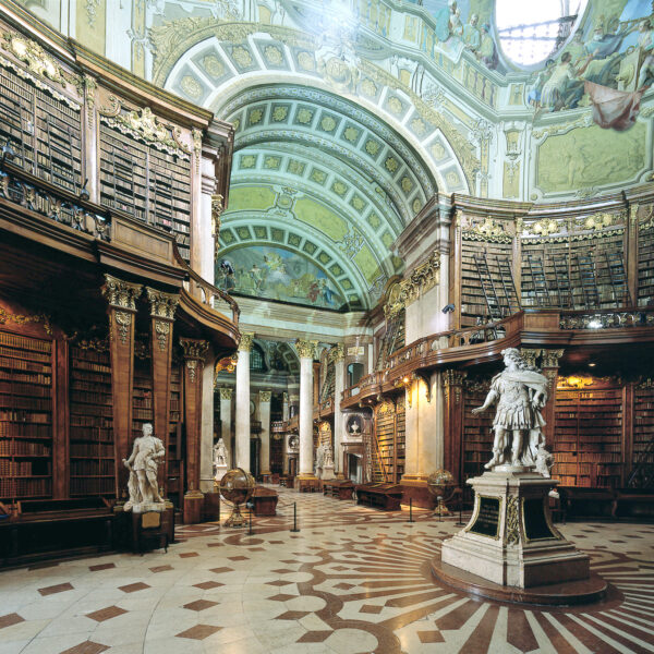 Große, verzierte Bibliothek mit hohen, gewölbten Decken, detaillierten Fresken, hohen Bücherregalen, Marmorstatuen und einem gemusterten Fußboden.