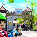 Eingang zum Playmobil FunPark mit großen Playmobil-Figurenstatuen, einem burgähnlichen Tor und Besuchern, die an einem sonnigen Tag eintreten.