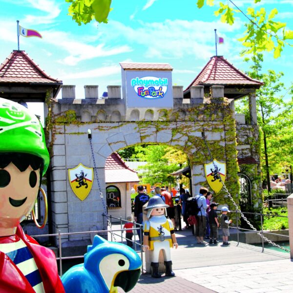 Eingang zum Playmobil FunPark mit großen Playmobil-Figurenstatuen, einem burgähnlichen Tor und Besuchern, die an einem sonnigen Tag eintreten.