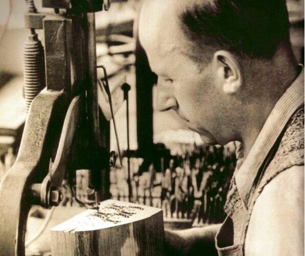 Ein Mann bedient eine mechanische Säge und schneidet in einer Werkstatt sorgfältig ein Muster in einen Holzblock.