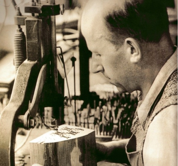 Ein Mann bedient eine mechanische Säge und schneidet in einer Werkstatt sorgfältig ein Muster in einen Holzblock.