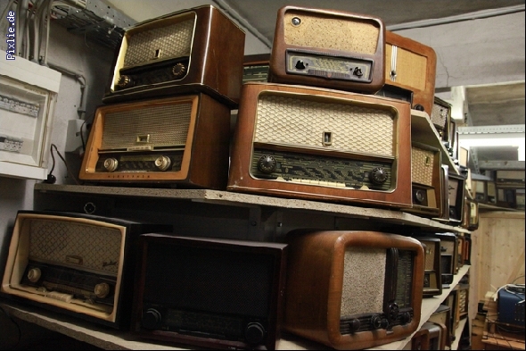 In einem Raum ist eine Sammlung von Vintage-Radios in verschiedenen Größen, Designs und Holzausführungen auf Regalen gestapelt.