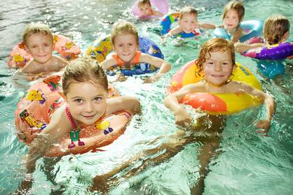 Eine Gruppe kleiner Kinder in Schwimmringen spielt zusammen in einem Schwimmbecken, lächelt und schaut in die Kamera.