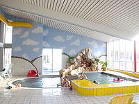 Kinder spielen in einem kleinen Hallenbad mit gelber Umrandung, Felsen und einem Wandgemälde mit Wolken an der Wand.