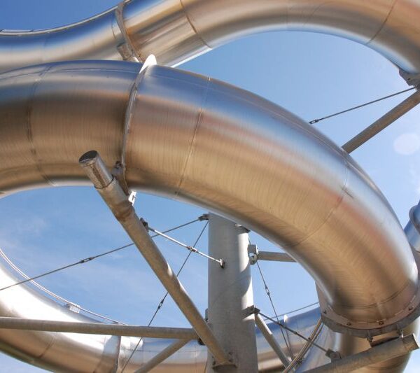 Gebogene Rohre aus rostfreiem Stahl, gestützt von Metallstäben und -trägern, vor einem klaren blauen Himmel.
