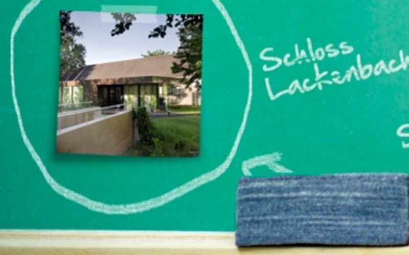 Auf einer grünen Kreidetafel ist das Foto eines Gebäudes aufgeklebt, umgeben von einem handgezeichneten Kreis aus Kreide neben einem mit Kreide geschriebenen Text und einem Radiergummi auf dem Kreidetablett.