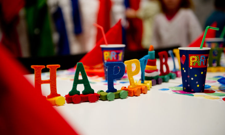Bunte Buchstaben mit der Aufschrift „HAPPY“ und dekorierte Becher mit Strohhalmen sind auf einem Tisch angeordnet und vermitteln den Eindruck einer festlichen Geburtstagsparty.