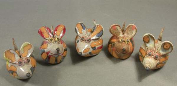 Fünf kleine, runde Steinskulpturen, die wie bunte Mäuse bemalt und verziert sind, stehen in einer Reihe auf einer grauen Fläche.