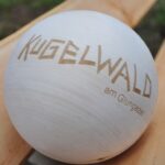 Eine glatte Holzkugel mit dem eingravierten Schriftzug "KUGELWALD am Glungezer", die auf einer hellen Holzfläche ruht.