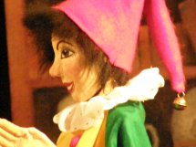 Nahaufnahme einer Marionette oder Puppe mit bemaltem Gesicht, die einen hellrosa spitzen Hut, ein grünes Kleid und einen weißen Rüschenkragen trägt.