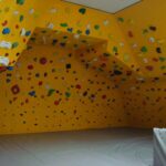 Indoor-Boulderwand mit gelben Platten und verschiedenfarbigen Klettergriffen, die mehrere Winkel abdecken, über einem gepolsterten Boden.