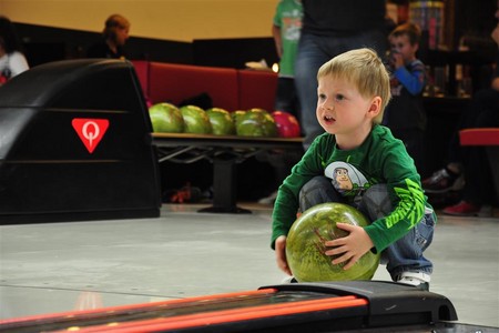 Ein Junge hockt und bereitet sich darauf vor, eine grüne Bowlingkugel die Bowlingbahn in einer Bowlinghalle hinunterzurollen.