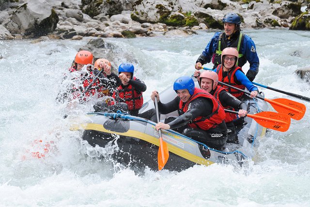 Eine Gruppe von sechs Personen, die Helme und Schwimmwesten tragen, paddelt auf einem Fluss durch plätschernde Wellen.