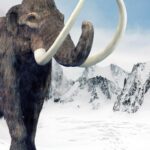 Ein Wollmammut mit langen gebogenen Stoßzähnen steht in einer verschneiten Berglandschaft unter einem teilweise bewölkten Himmel.