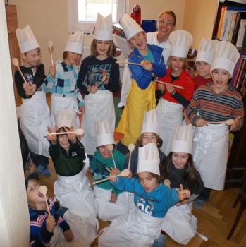 Eine Gruppe von Kindern mit Kochmützen und Schürzen posiert im Haus mit Kochlöffeln, begleitet von einem Erwachsenen, der ebenfalls als Koch gekleidet ist.