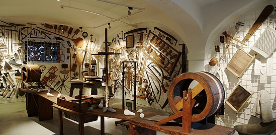 In einem Ausstellungsraum des Museums sind verschiedene alte Werkzeuge und landwirtschaftliche Geräte aus Holz an den Wänden und auf Tischen ausgestellt.