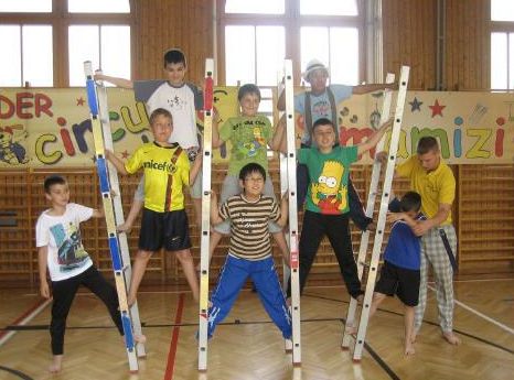 Eine Gruppe von Jungen balanciert in einer Turnhalle auf und zwischen hölzernen Leitern und posiert gemeinsam für ein Gruppenfoto.