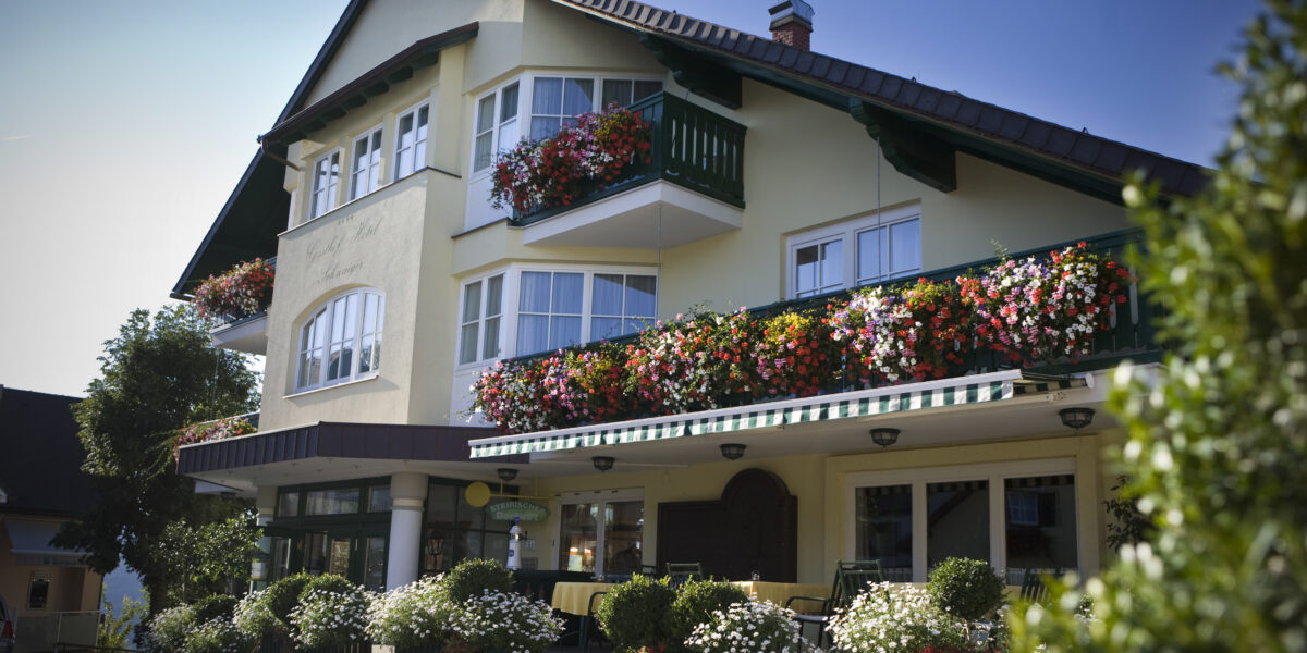 Ein dreistöckiges Haus mit Balkonen und Fenstern, die mit bunten Blumenkästen und grünen Geländern geschmückt sind, unter einem klaren blauen Himmel.