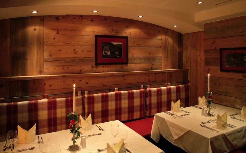 Ein gemütlicher Restaurantbereich mit Holzwänden, gepolsterten Sitzen, gedeckten Tischen mit weißen Tüchern, Kerzen und gerahmten Bildern an den Wänden.