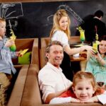 Eine Familie sitzt zusammen in einem Restaurant, lächelt und genießt die Getränke, während ein Kellner einem der Erwachsenen einen Cocktail reicht.