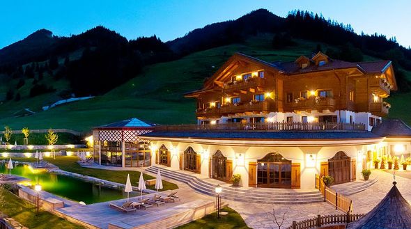 Ein großes Hotel im Chalet-Stil mit Balkonen, Außenpool, Sitzgelegenheiten auf der Terrasse und Bergblick in der Abenddämmerung.