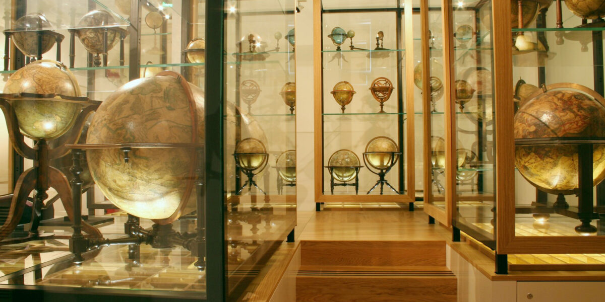Eine museale Ausstellung antiker Globen in Glasvitrinen auf Holzpodesten, die verschiedene Größen und historische Kartendesigns zeigen.