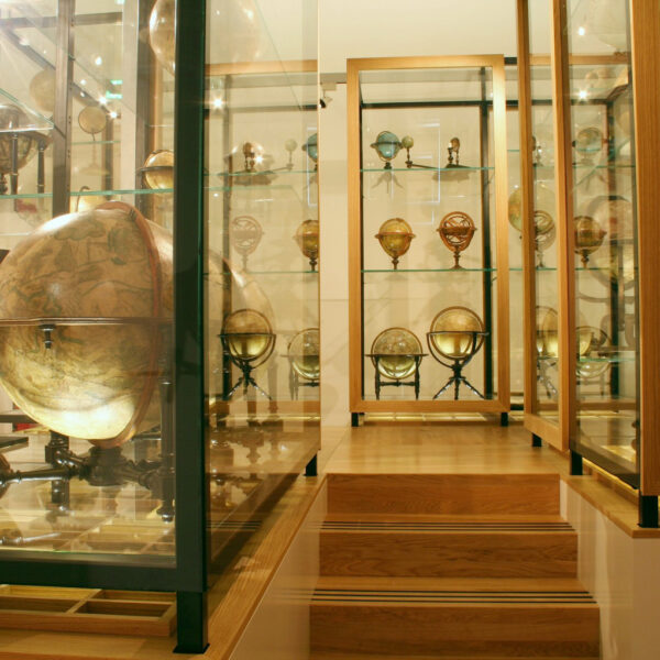 Eine museale Ausstellung antiker Globen in Glasvitrinen auf Holzpodesten, die verschiedene Größen und historische Kartendesigns zeigen.