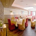 Ein helles, modernes Restaurant mit Stein- und Holzakzenten, weiß gedeckten Tischen und Stühlen mit rot-gelb kariertem Stoff.