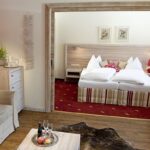 Moderne Hotelsuite mit einem Wohnbereich mit Sofa und Couchtisch und einem Schlafzimmer mit zwei Einzelbetten, roten Akzenten und dekorativen Kissen.