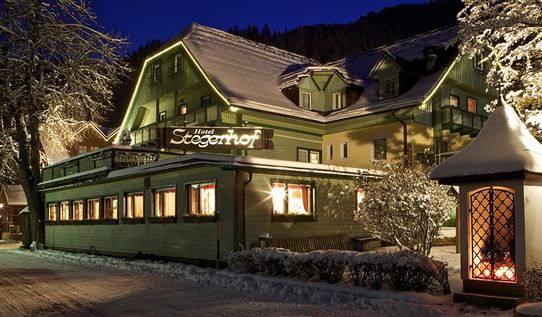 Ein verschneites Hotel namens Stegenhof ist nachts beleuchtet, mit warmen Lichtern aus den Fenstern und schneebedeckten Bäumen, die das Gebäude umgeben.