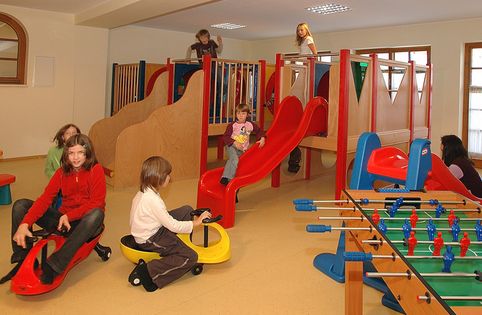 In einem Indoor-Spielzimmer mit Holzspielgeräten können die Kinder auf Rutschen, Fahrgeräten und einem Kickertisch spielen.