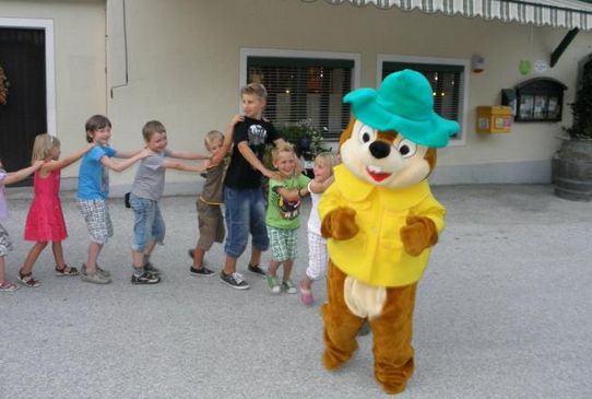 Eine Person in einem Cartoon-Streifenhörnchen-Kostüm führt eine Reihe von Kindern an, die sich vor einem Gebäude aneinander festhalten.