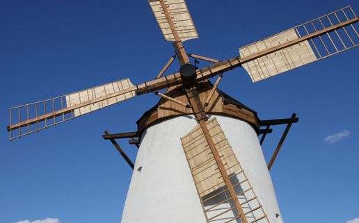 Eine traditionelle weiße Windmühle mit hölzernen Flügeln steht vor einem klaren blauen Himmel.