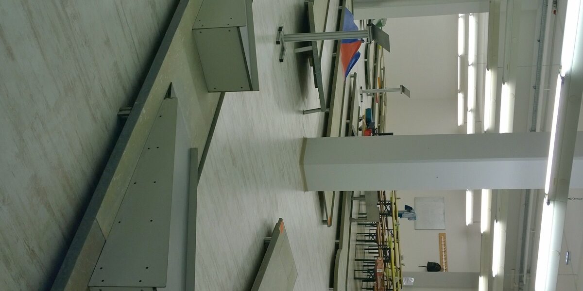 Eine Indoor-Minigolfanlage mit mehreren Bahnen, Hindernissen und Tischen in einem hell erleuchteten Raum mit weißen Wänden und Deckenleuchten.